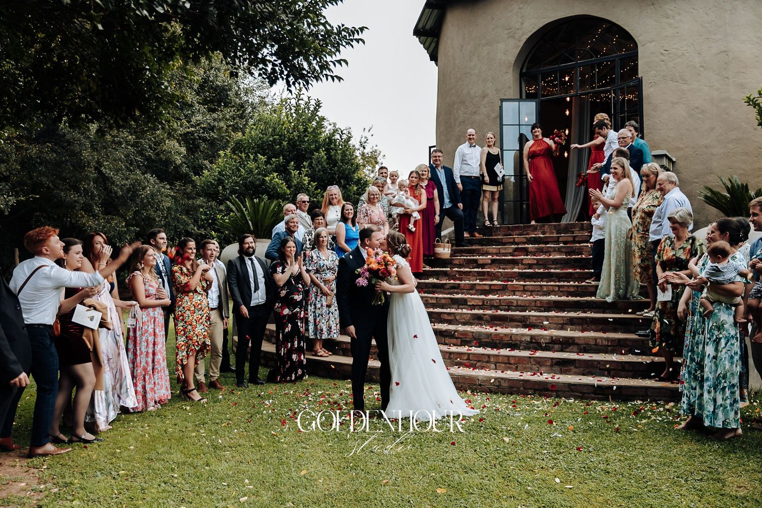 Newlyweds celebrated by guests throwing confetti on stone steps outside a chapel.