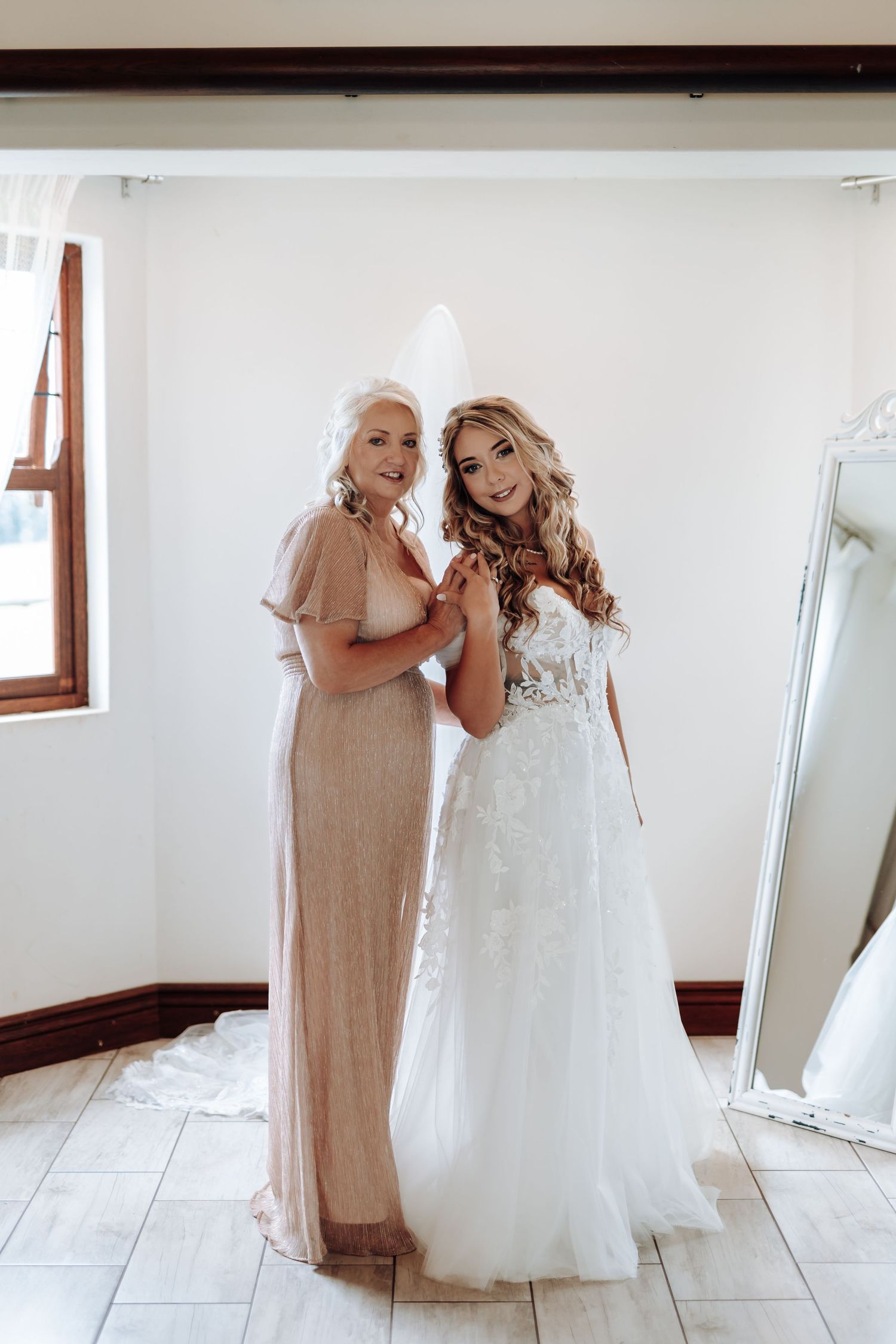 Two women share an emotional moment while getting ready for a wedding in a bright white room.