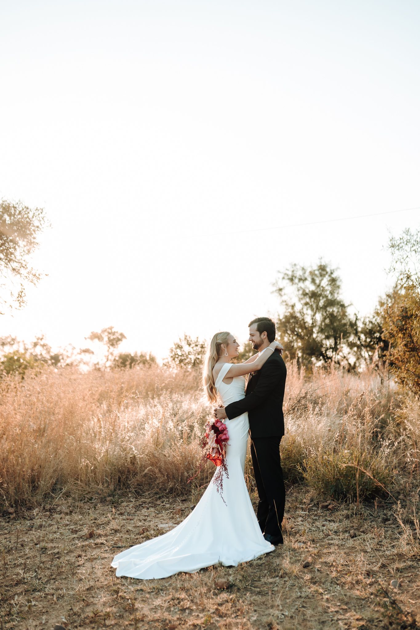 Intimate wedding portrait of couple in warm evening light against dried grass landscape.