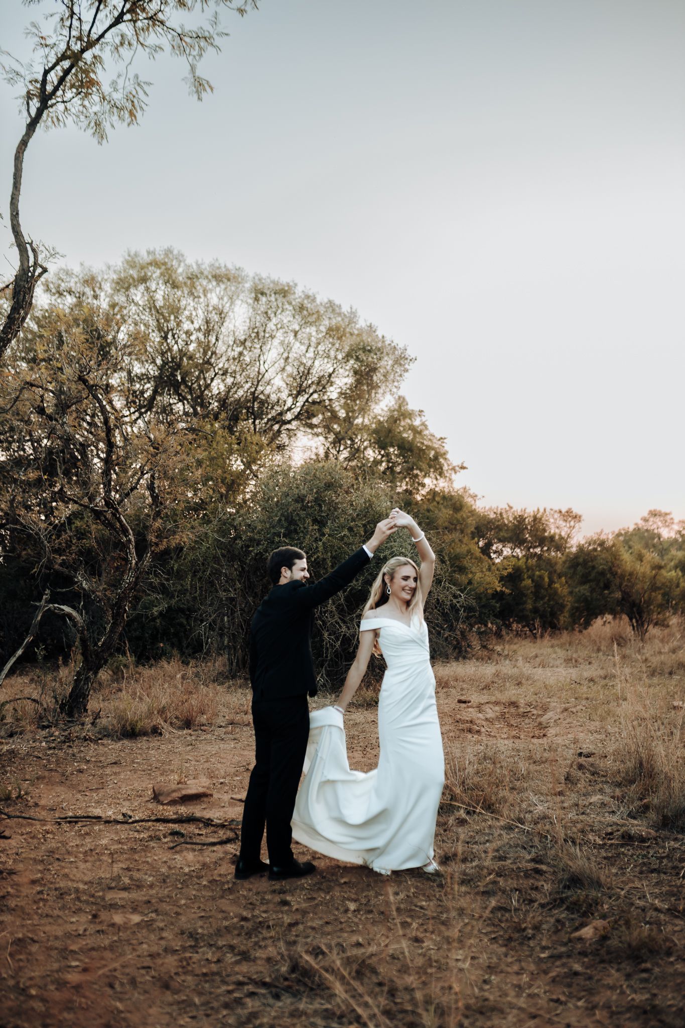A couple dances in a natural setting with trees in the background.