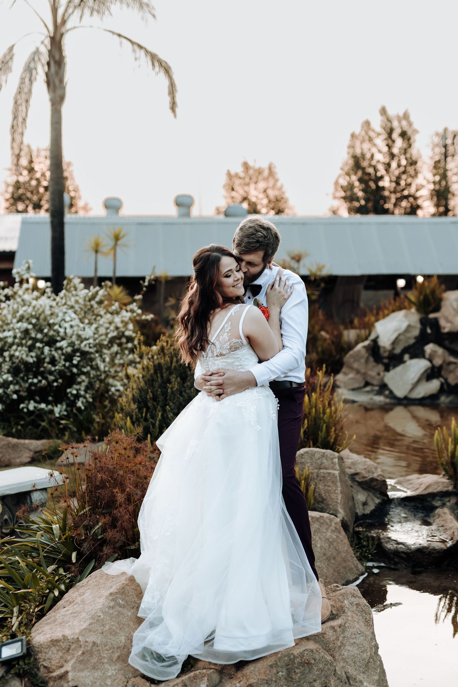 Romantic wedding photo of couple sharing tender moment among garden landscaping and rocks.