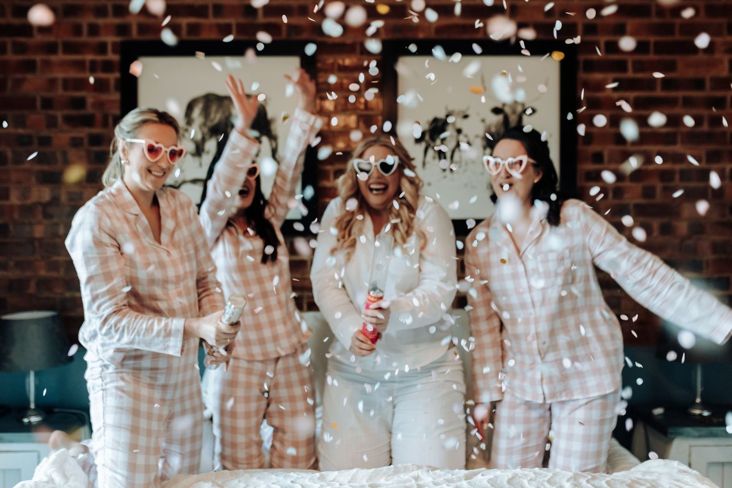 Friends in matching sleepwear celebrate with confetti in front of rustic wall decor.