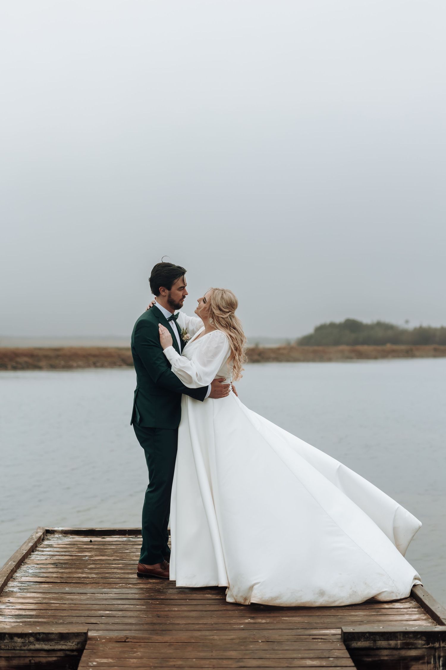 Couple shares intimate moment on wooden dock overlooking coastal waters.