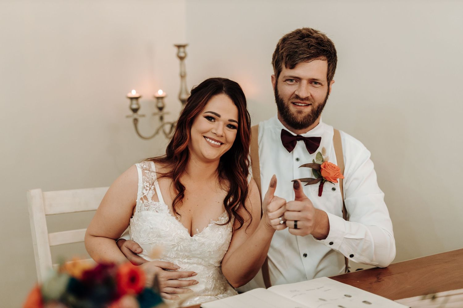 Newlyweds sharing drinks at rustic reception table with candelabra.