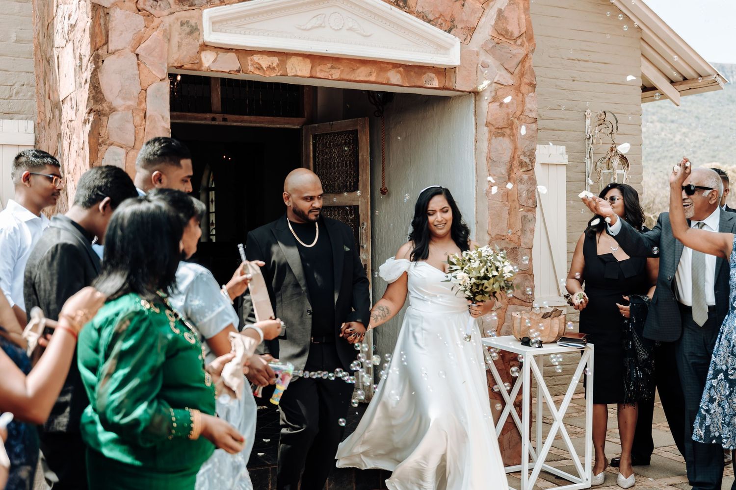 Wedding couple exits venue while guests celebrate with confetti and lantern decorations.