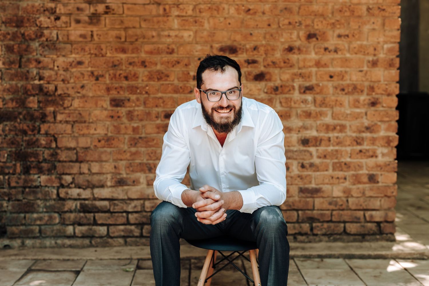 Casual business portrait against rustic brick wall with natural lighting and modern seating.