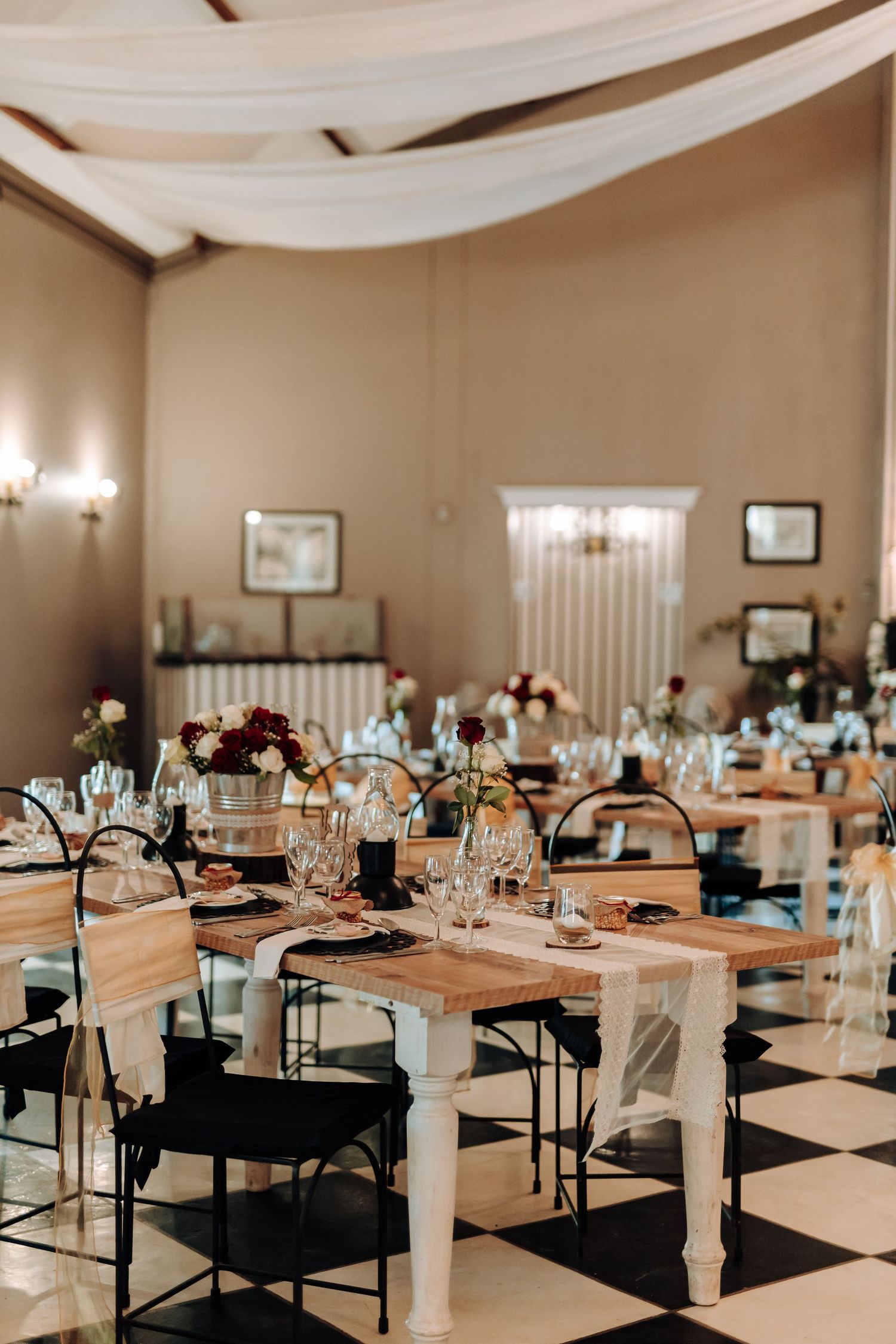 Elegant wedding reception venue with draped fabric, wooden tables and black chairs.