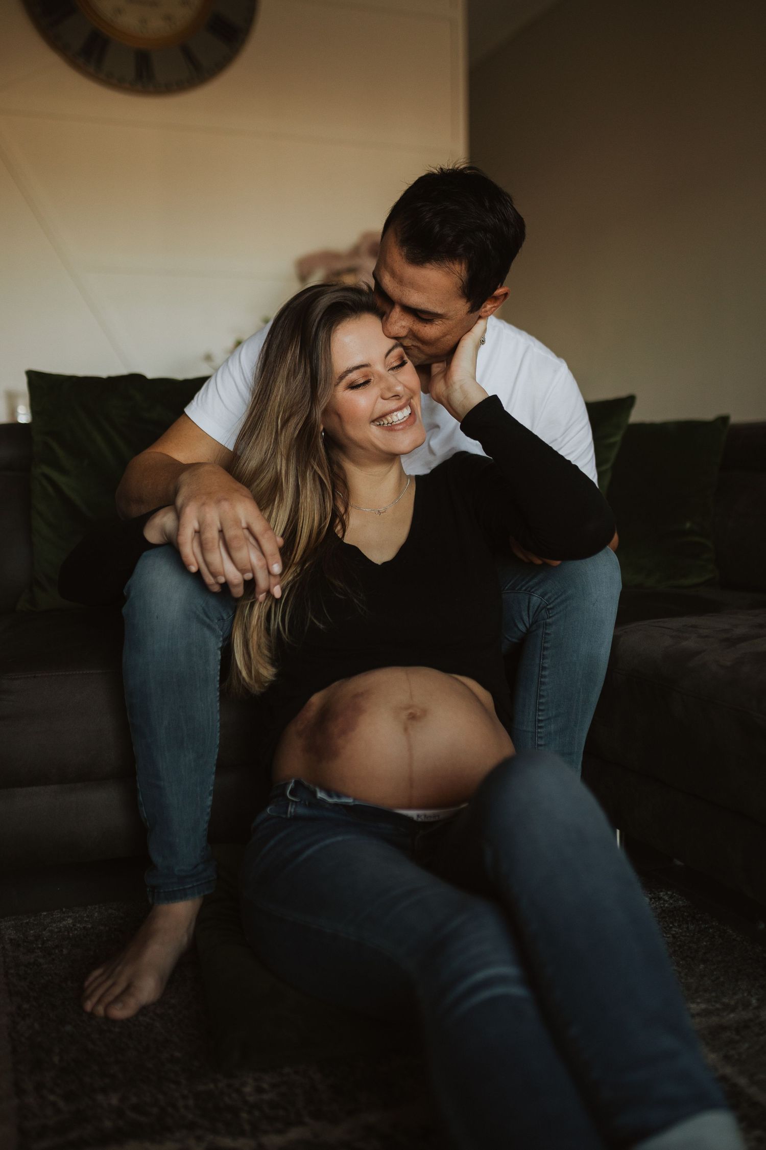 Intimate couple share tender moments together on a dark couch during lifestyle photography session.