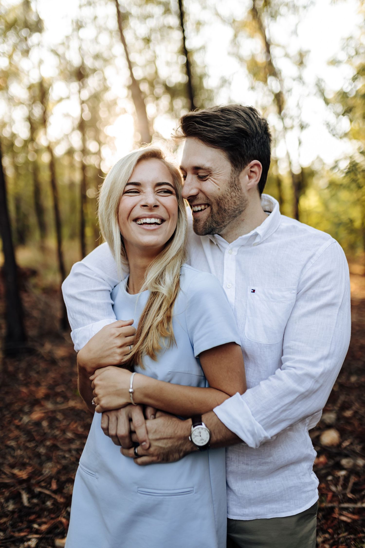 Happy couple embracing and laughing together in a sunlit forest during golden hour.