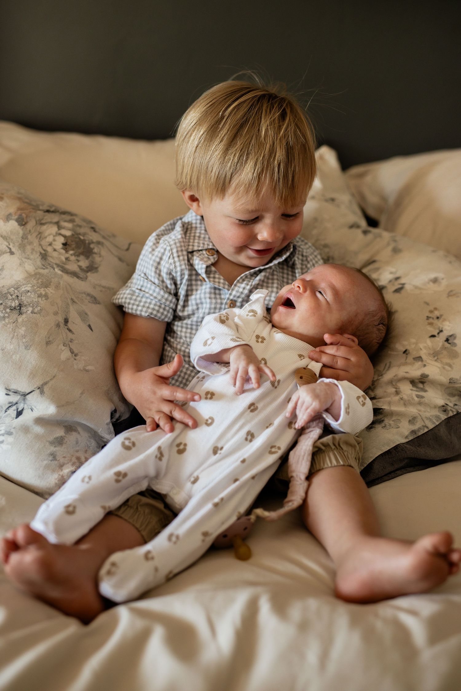 Siblings share a tender bonding moment while cuddling together on white bedding.