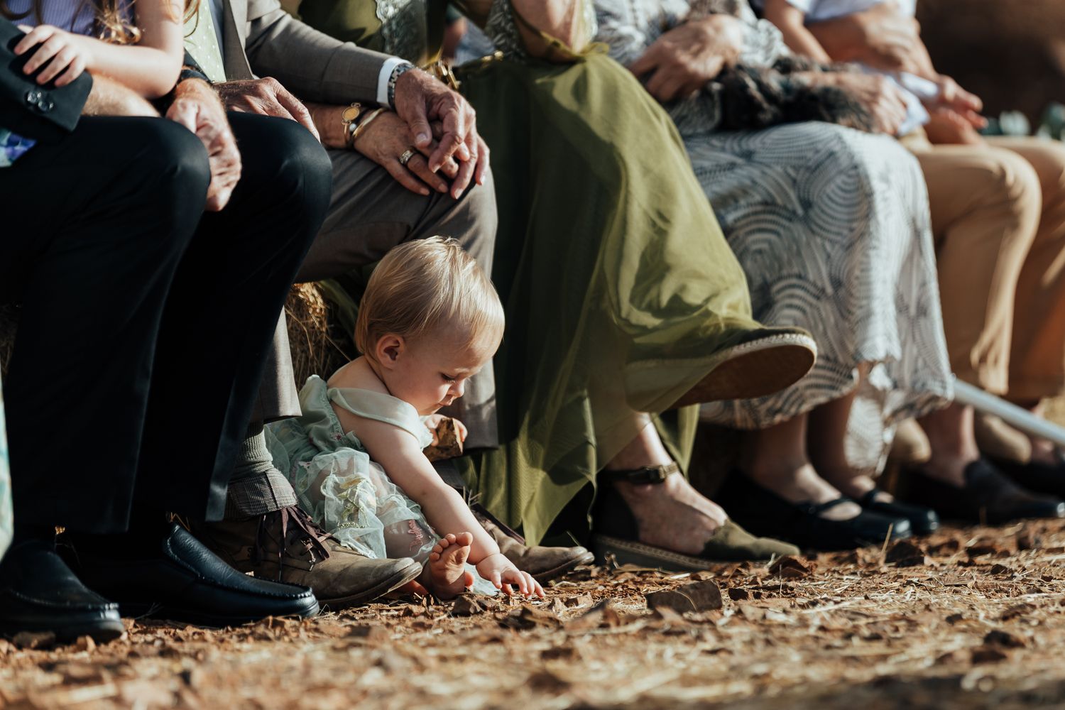 Young child plays in dirt during outdoor wedding ceremony seating.