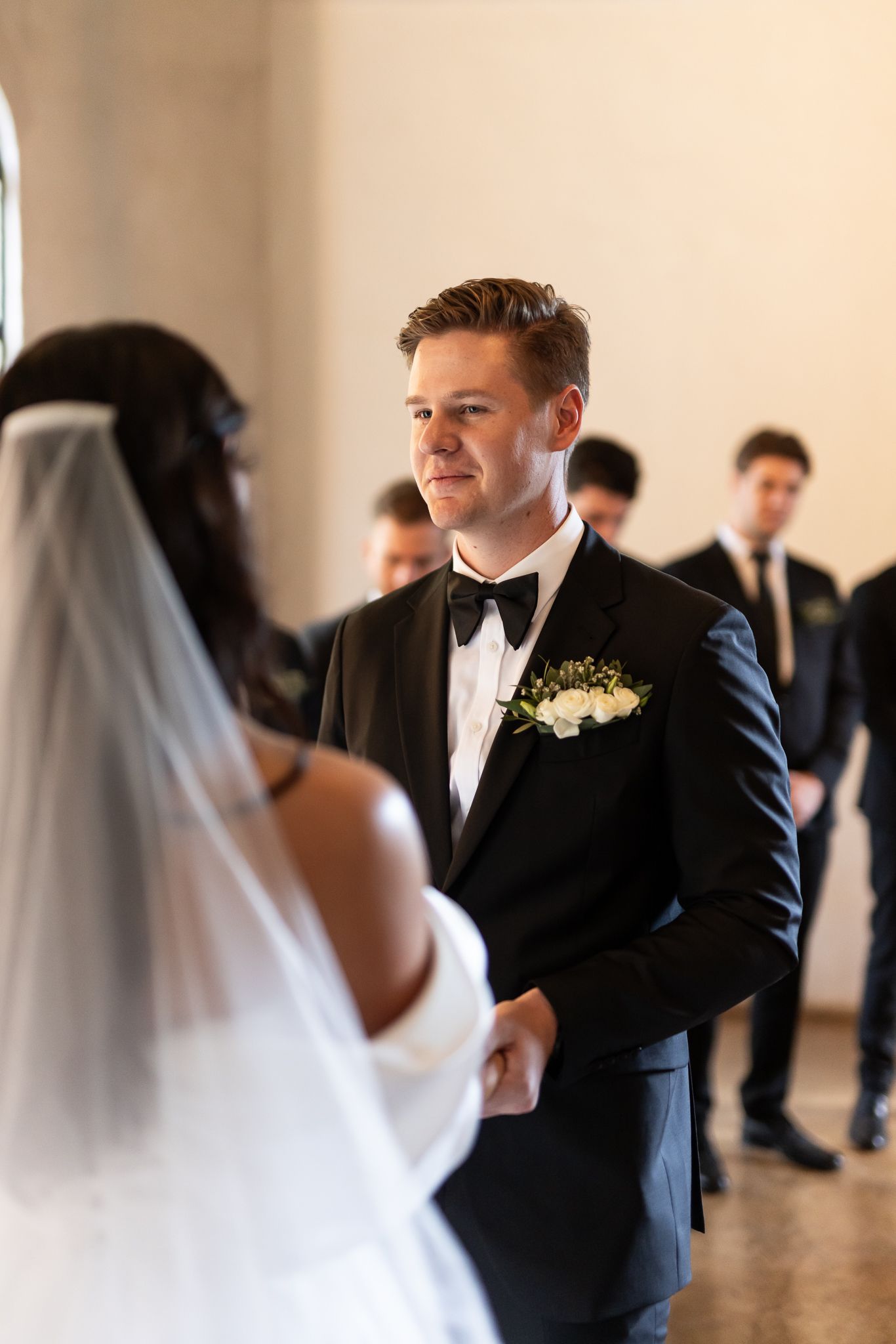 A couple during their wedding ceremony in a sunlit room with elegant decor.