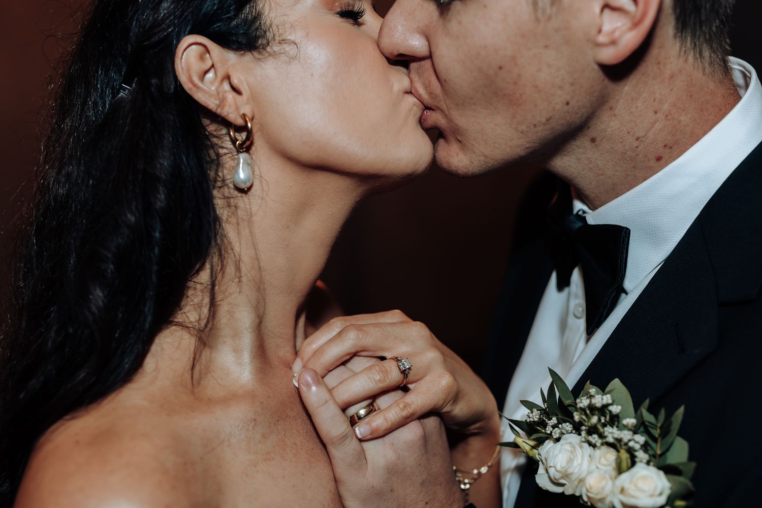 A close-up wedding portrait showing a romantic kiss and sparkling engagement ring.