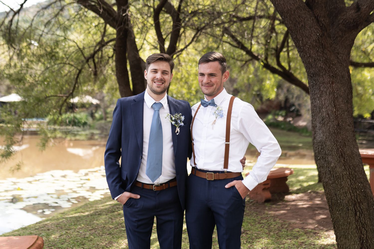 Two groomsmen in contrasting navy suit and white shirt with suspenders outdoors.