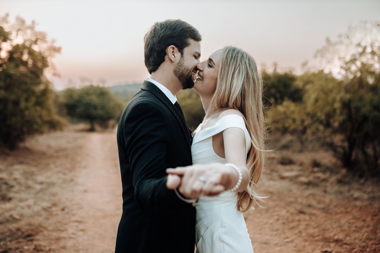A tender moment between newlyweds embracing on a rustic dirt path at sunset.