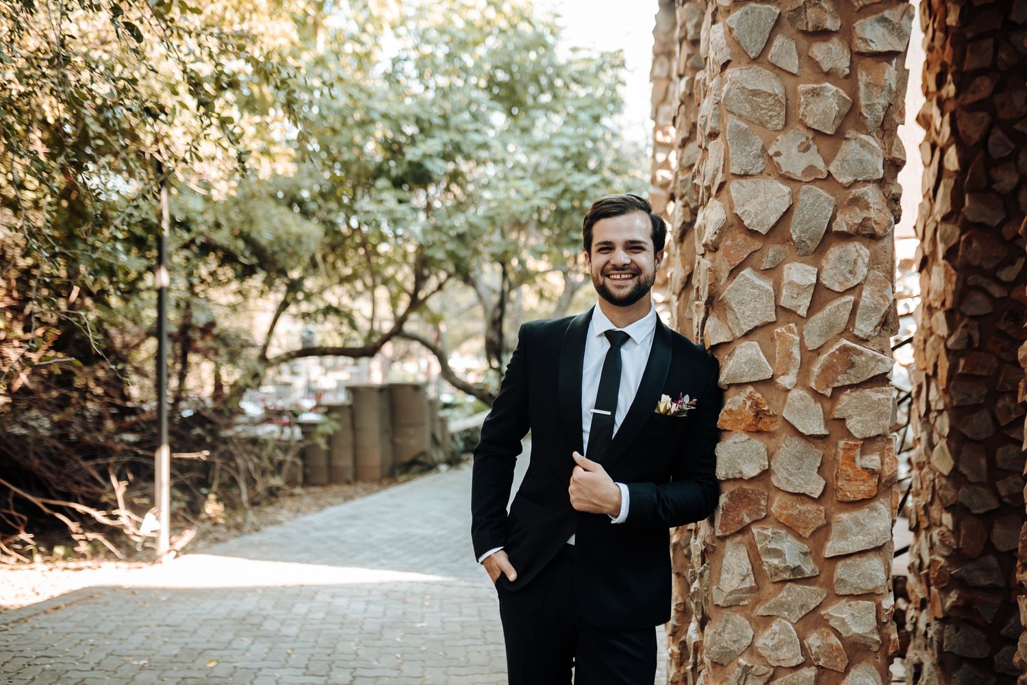 Elegant portrait beside stone columns with sunlit garden path in background.