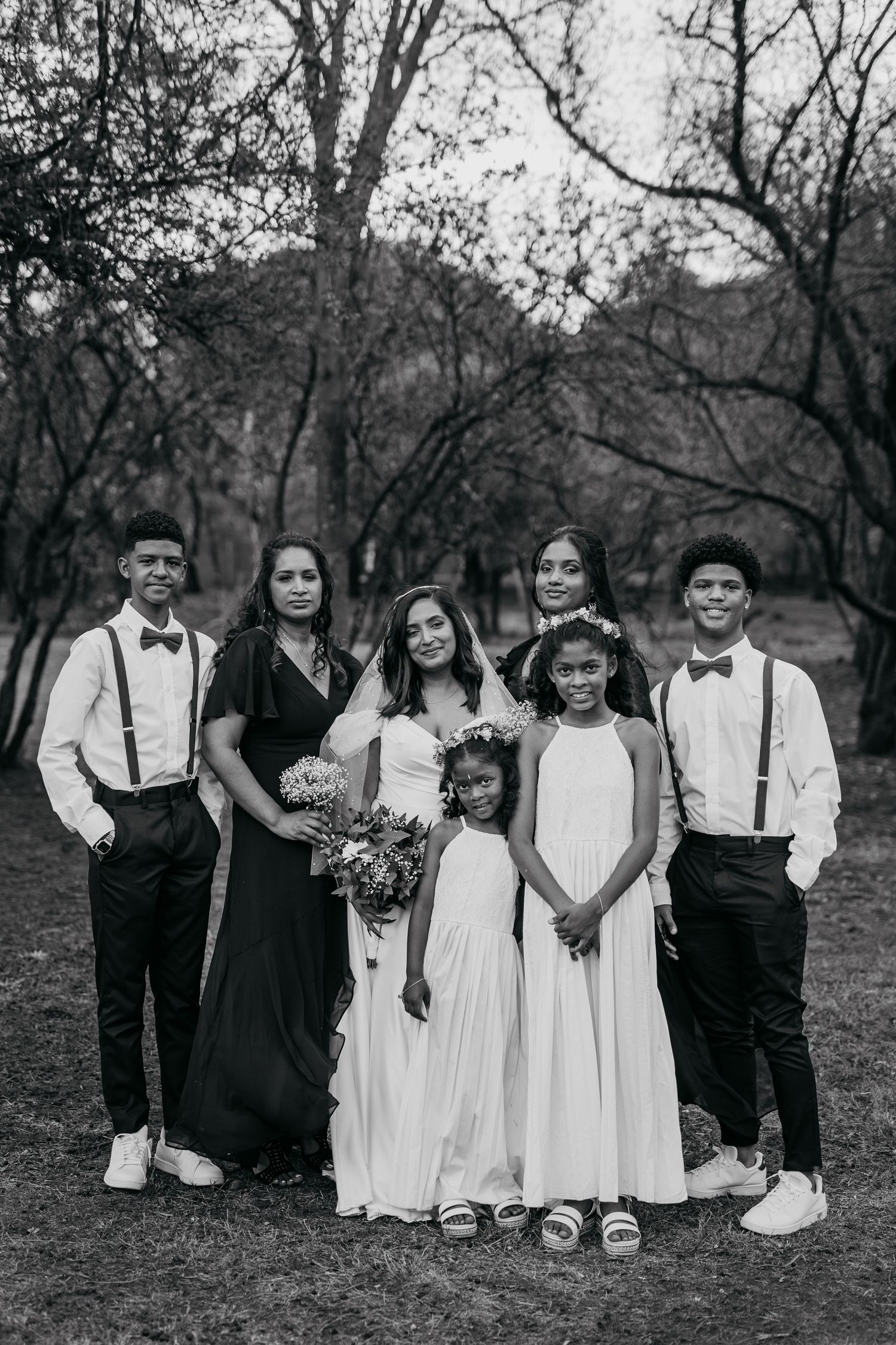 Black and white photo of wedding party in coordinated attire posing outdoors.