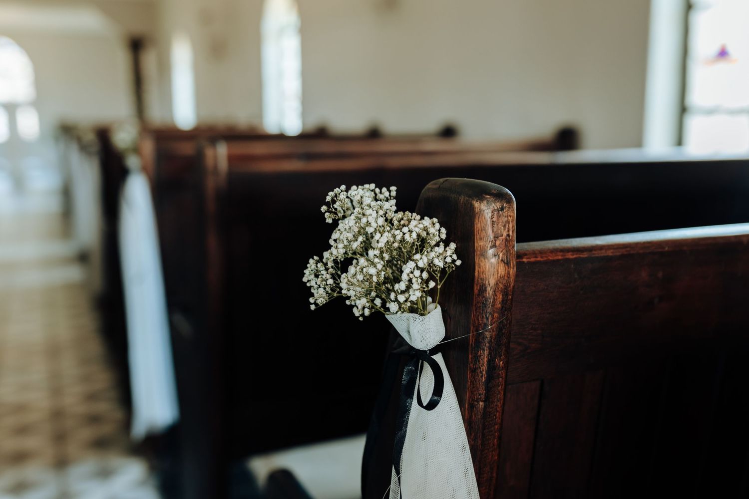 Baby's breath flower bouquet tied with black ribbon decorating church pew end.