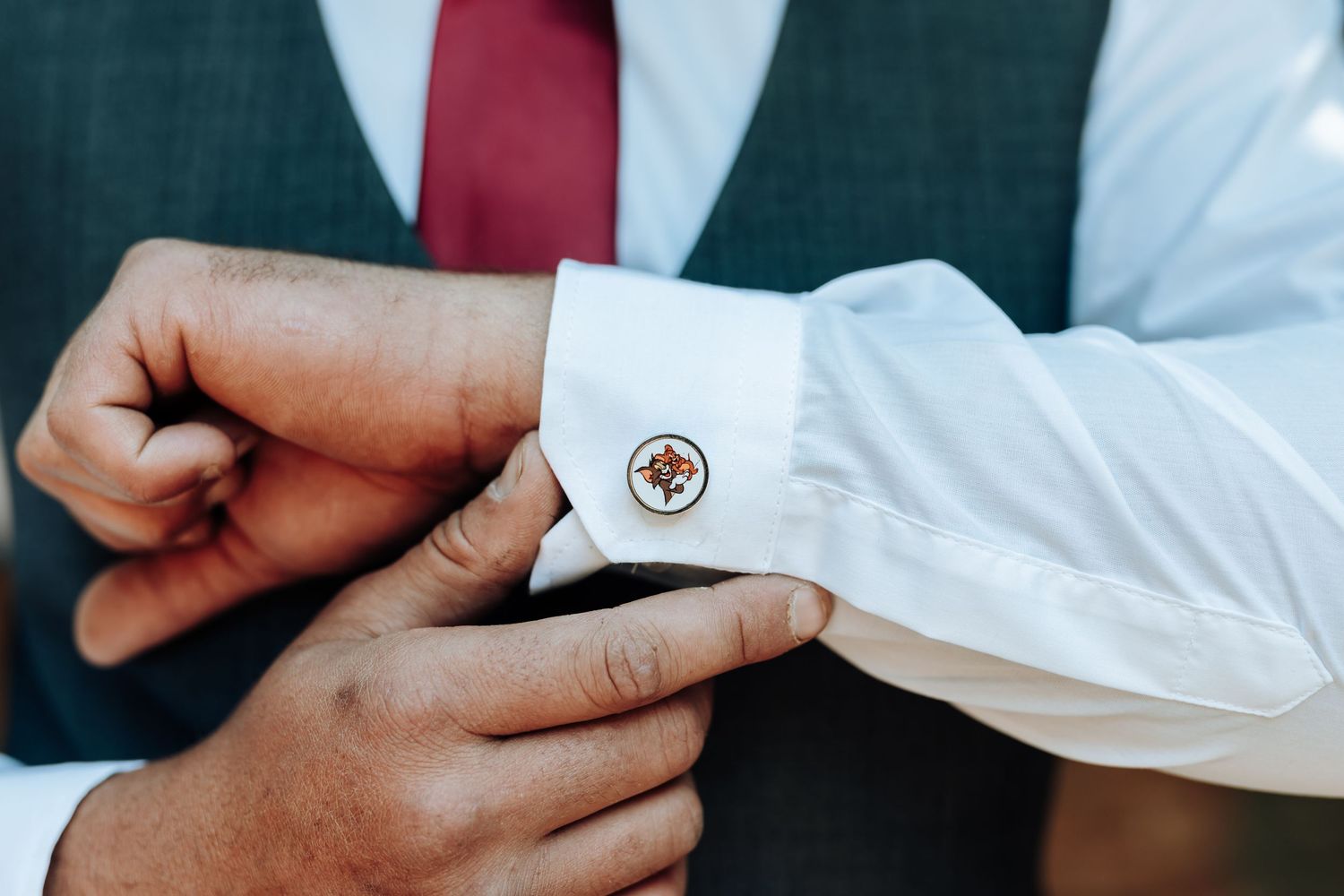 Detailed shot of hands fastening decorative cufflink on white shirt cuff.