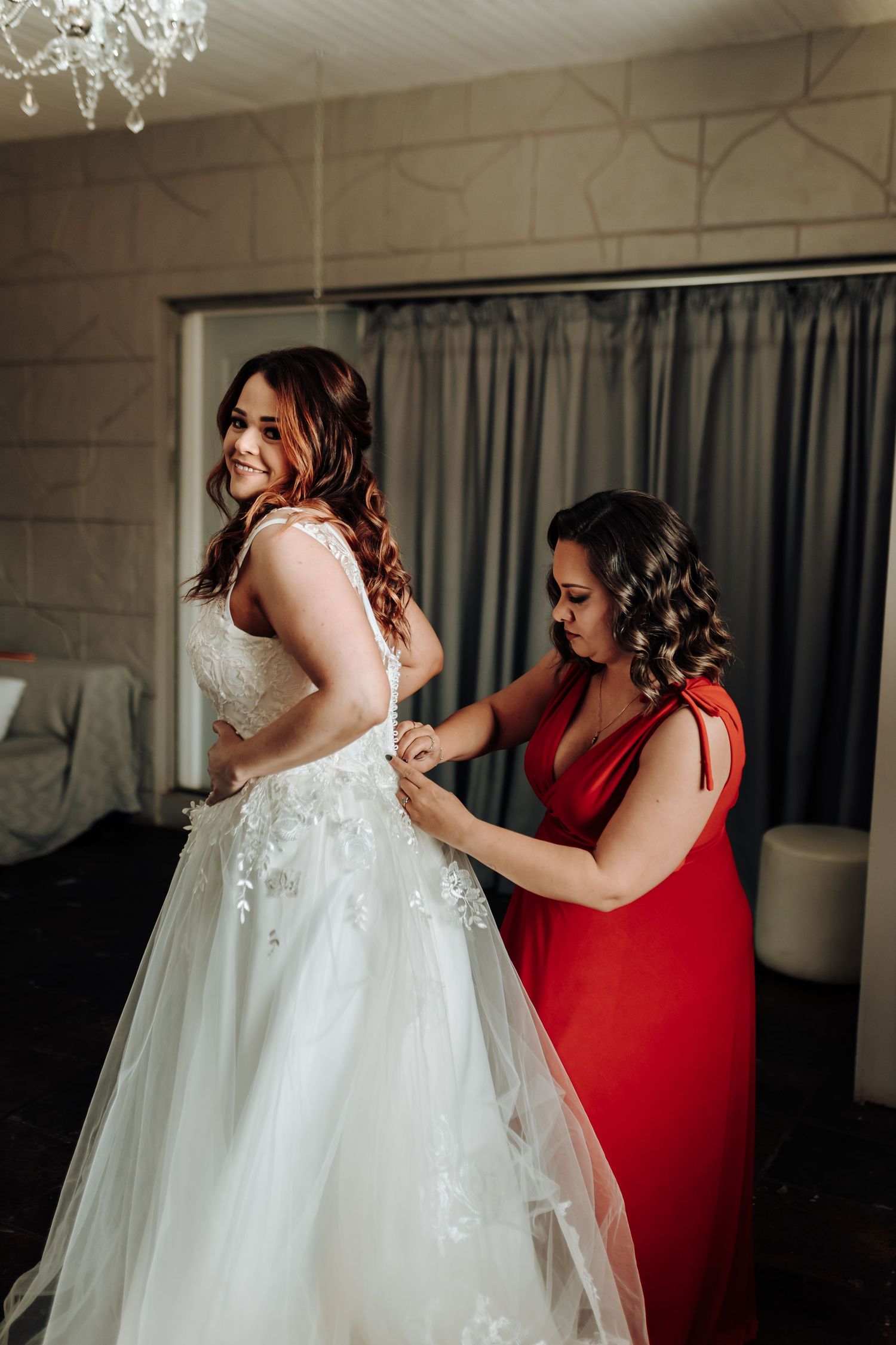 A wedding dress being laced up in an elegant room with a chandelier overhead.