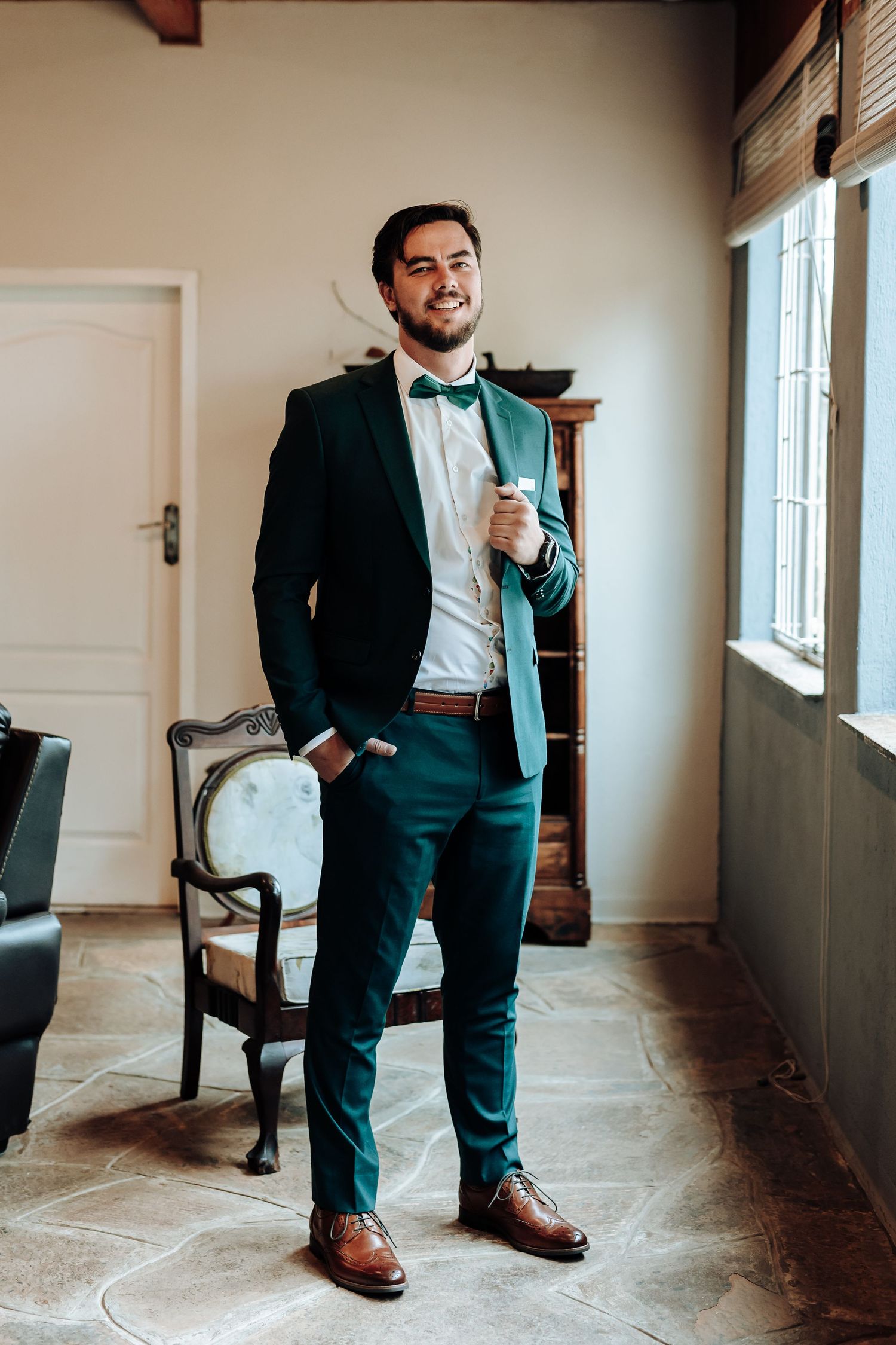 Stylish emerald green suit with bow tie and brown leather accessories in formal setting.