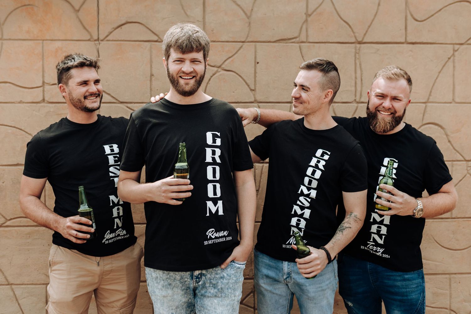 Group showing off their matching black graphic t-shirts while holding beverages.