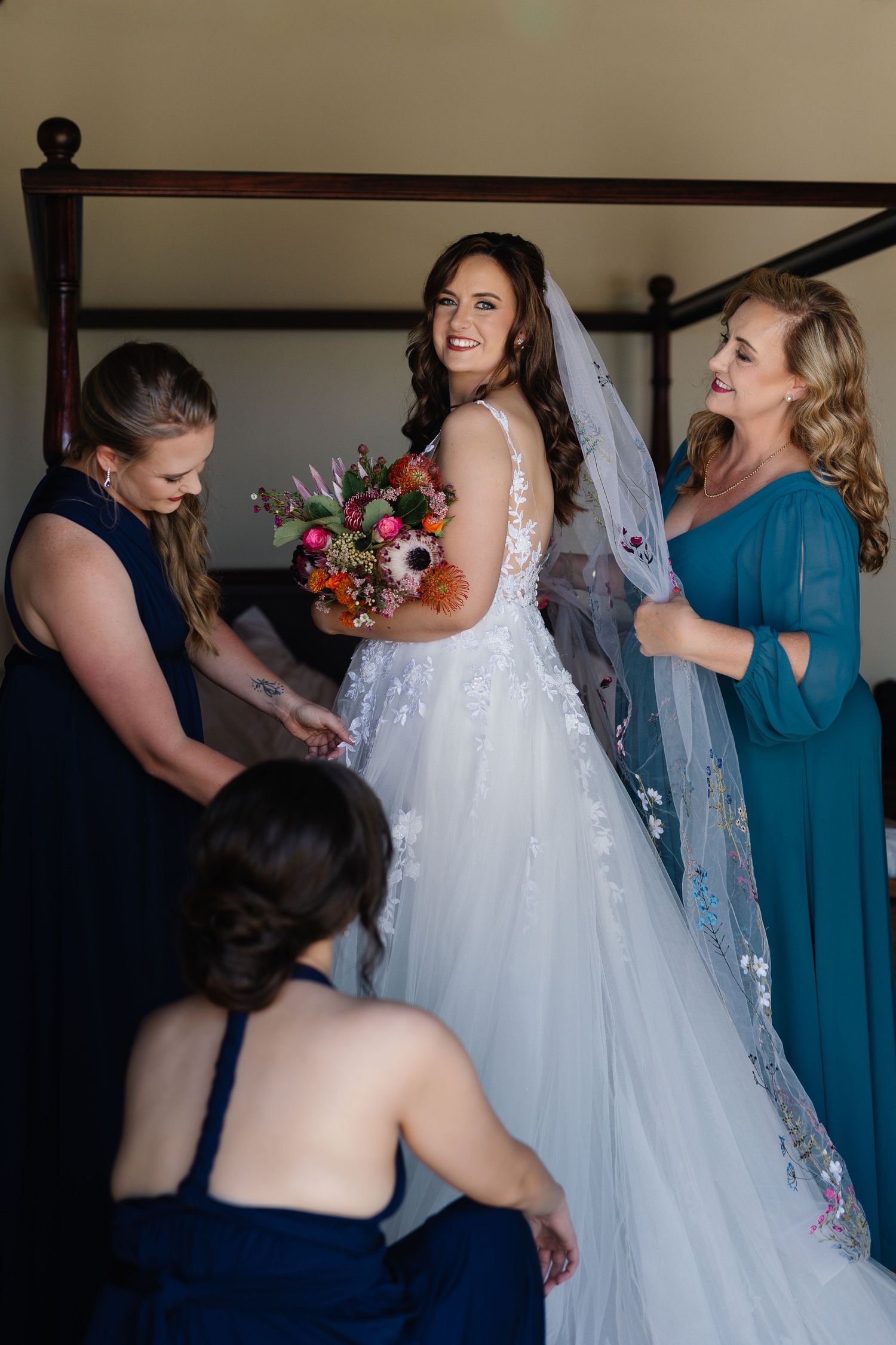 A group helps the bride get dressed in her flowing white wedding gown with lace details.