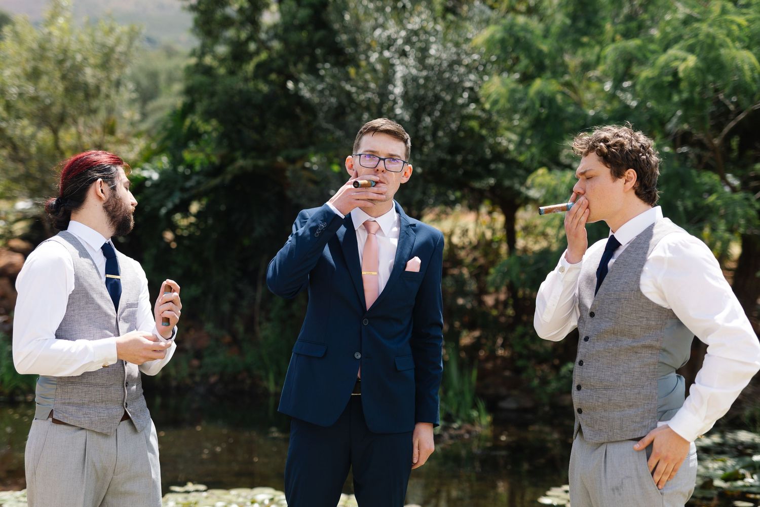 Three people in formal attire share a lighthearted moment during an outdoor celebration in a garden setting.