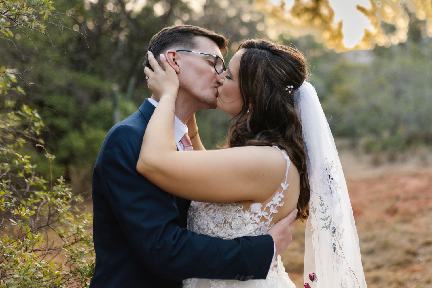 A romantic couple in wedding attire share intimate moments in a sunlit outdoor setting during golden hour.