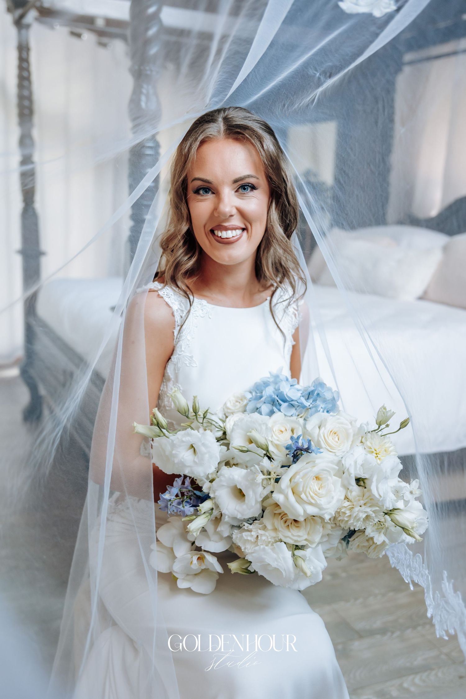 Elegant bridal portrait featuring a white wedding bouquet with roses and blue accents against a light background.
