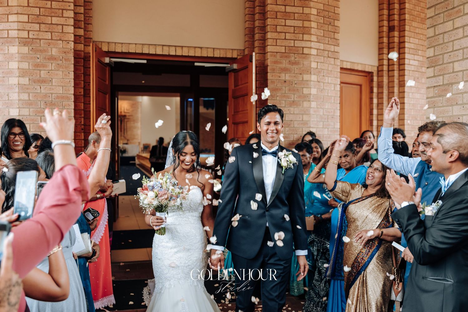 Wedding ceremony exit with guests celebrating and throwing confetti outside brick church.