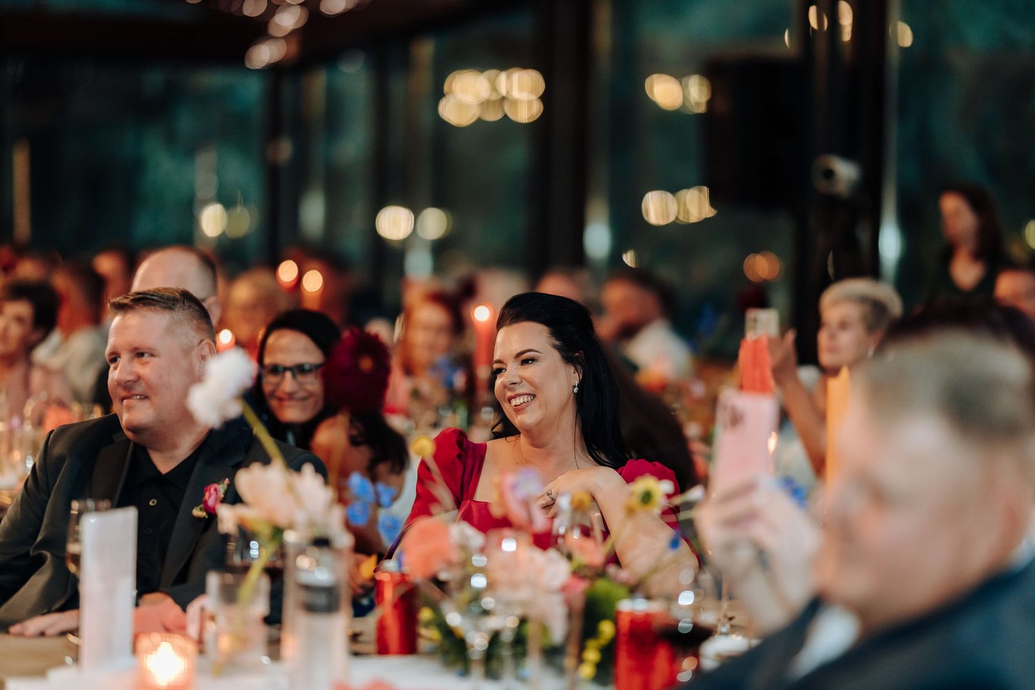 Reception venue with soft bokeh lighting and guests seated at decorated tables for a celebration.