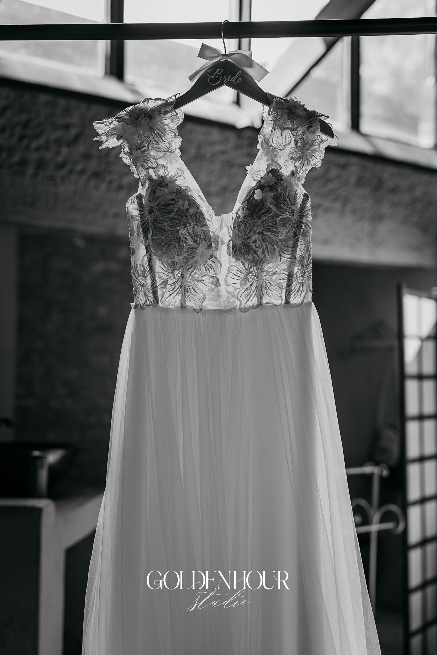 Elegant bridal gown with lace bodice and flowing tulle skirt hanging on a Bride hanger in black and white.
