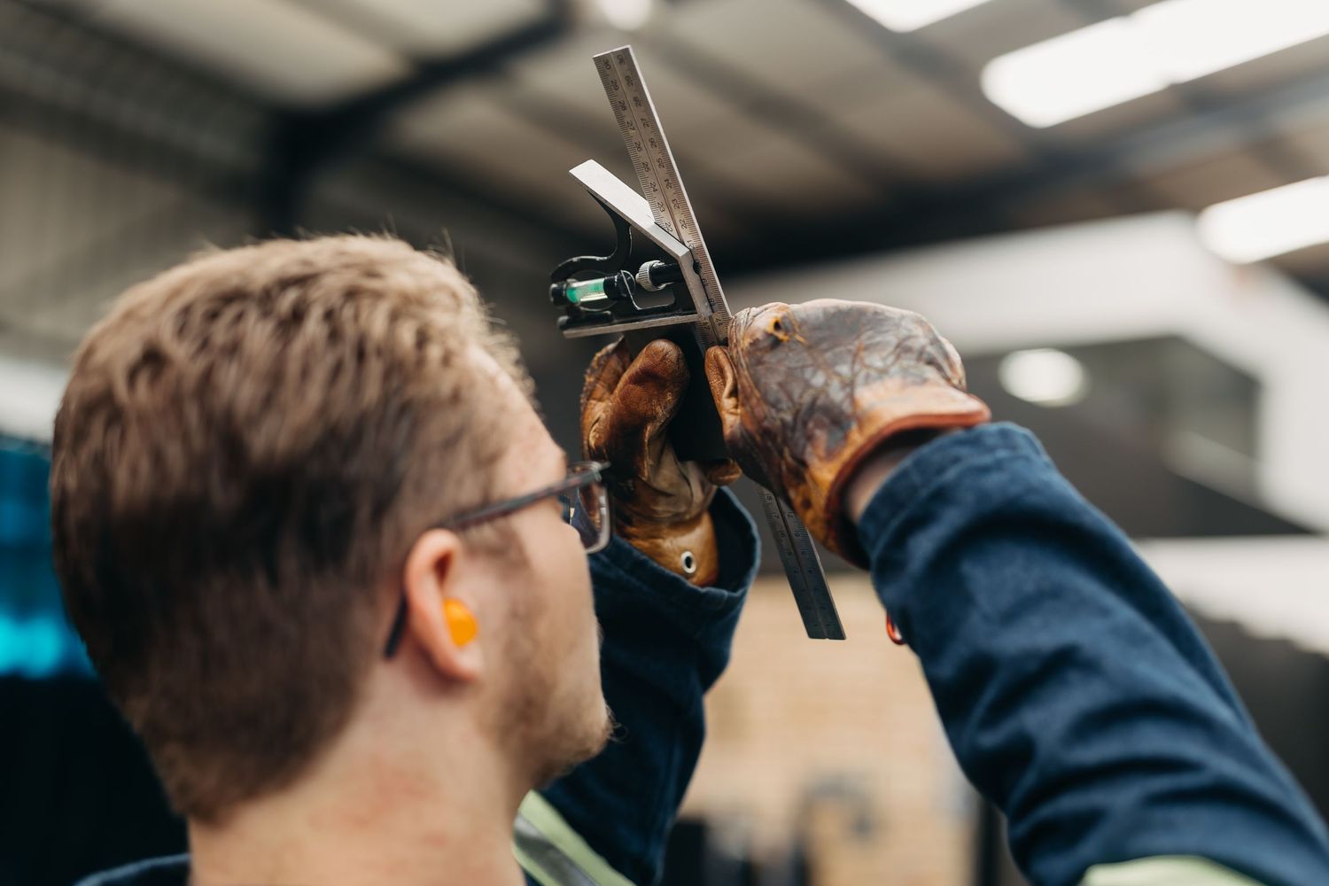 Two workers in protective equipment inspect machinery components in a factory setting.