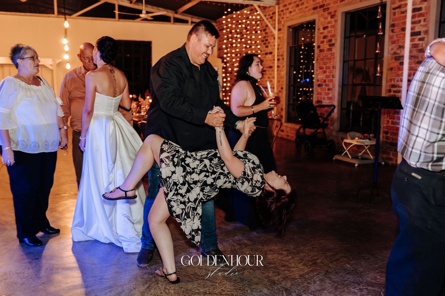 Guests dance energetically on wedding reception dance floor with bride visible in white gown nearby.