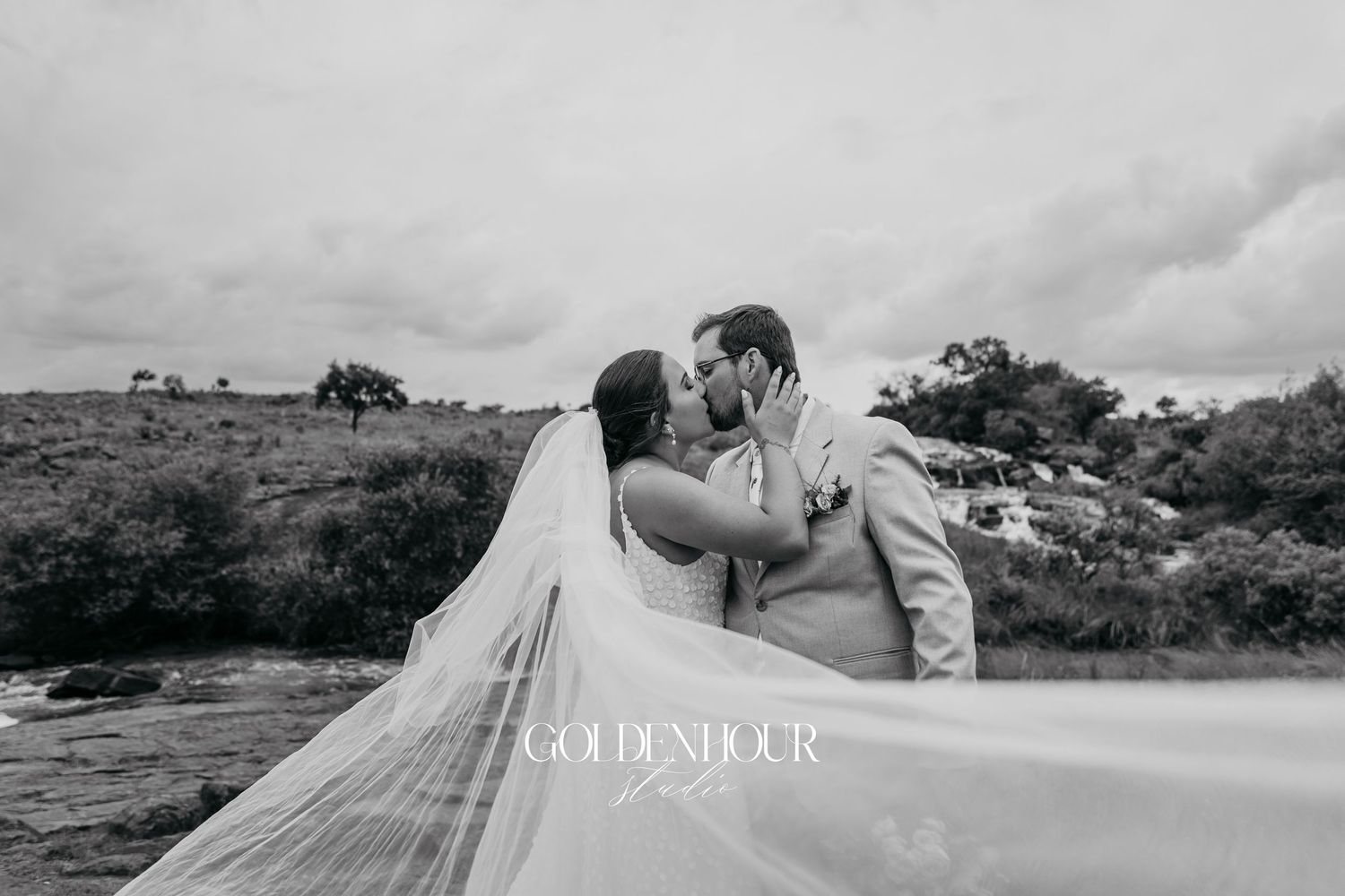 A dreamy wedding photo captured in a vast field with mountains and dramatic clouds in the background.