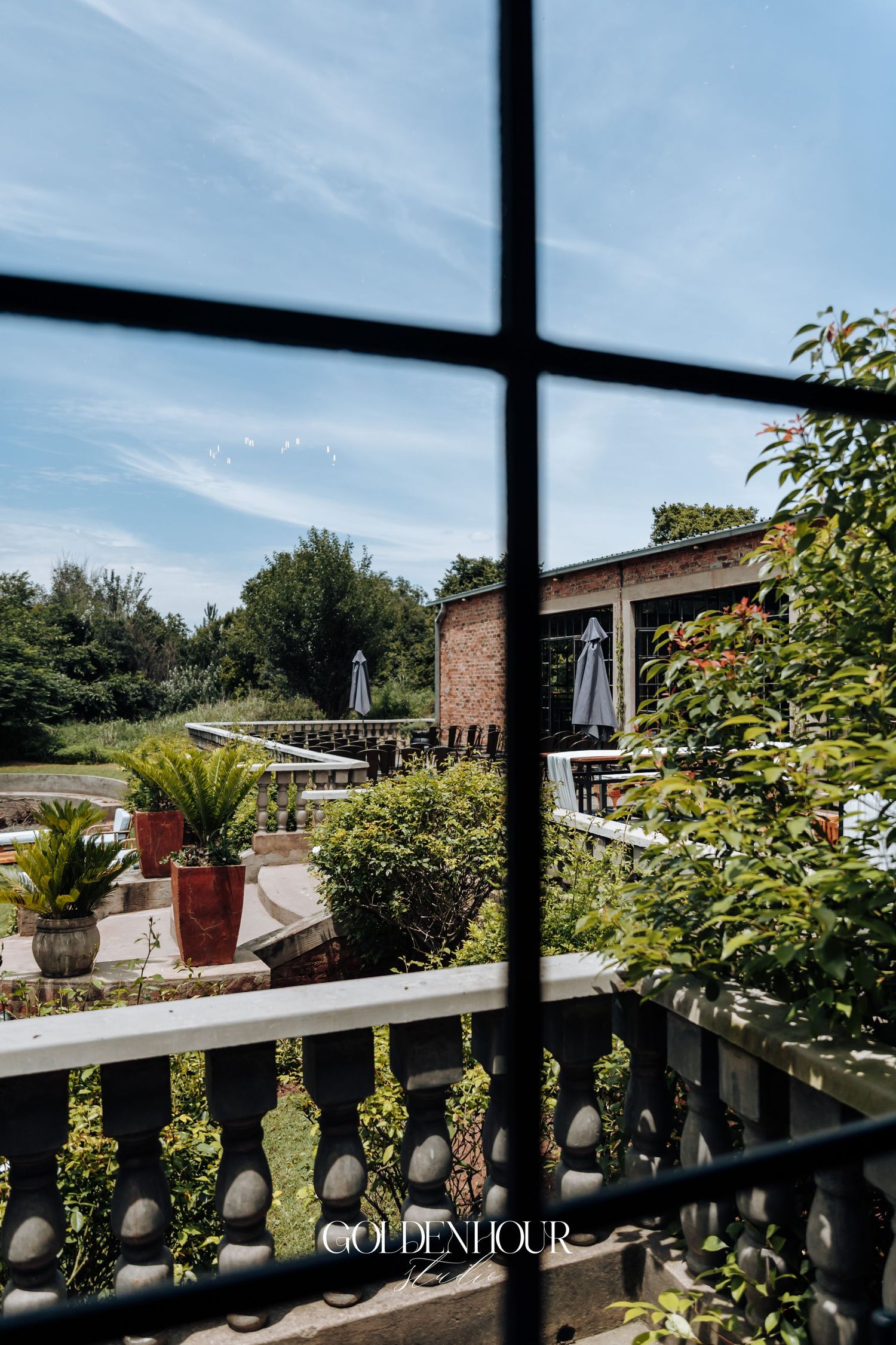View through window of outdoor terrace with stone balustrade and lush garden landscape.