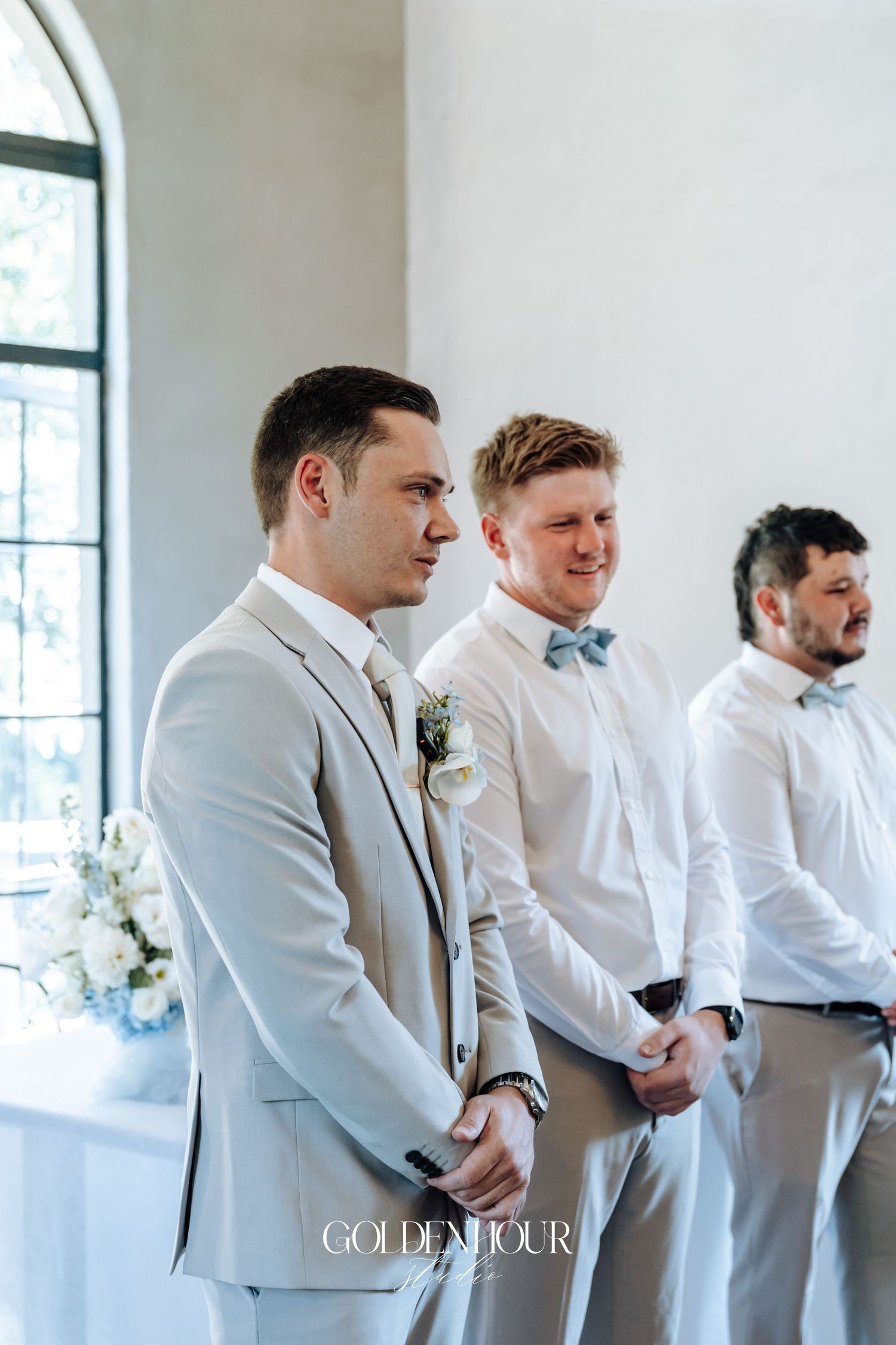 Groomsmen in light gray suits and white shirts lined up during wedding ceremony.
