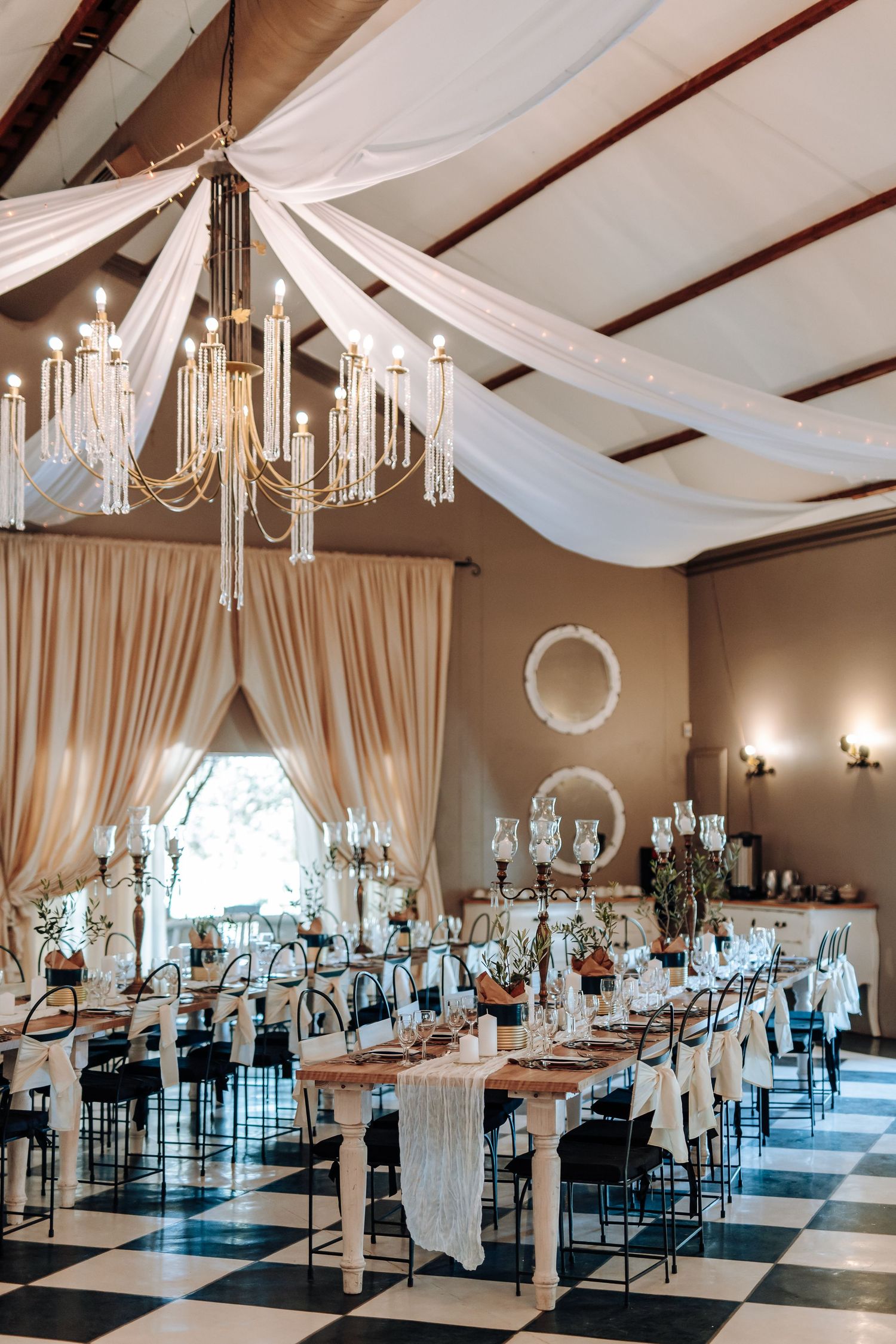 Elegant wedding reception venue with white draping, crystal chandeliers and turquoise accents in a spacious ballroom setting.
