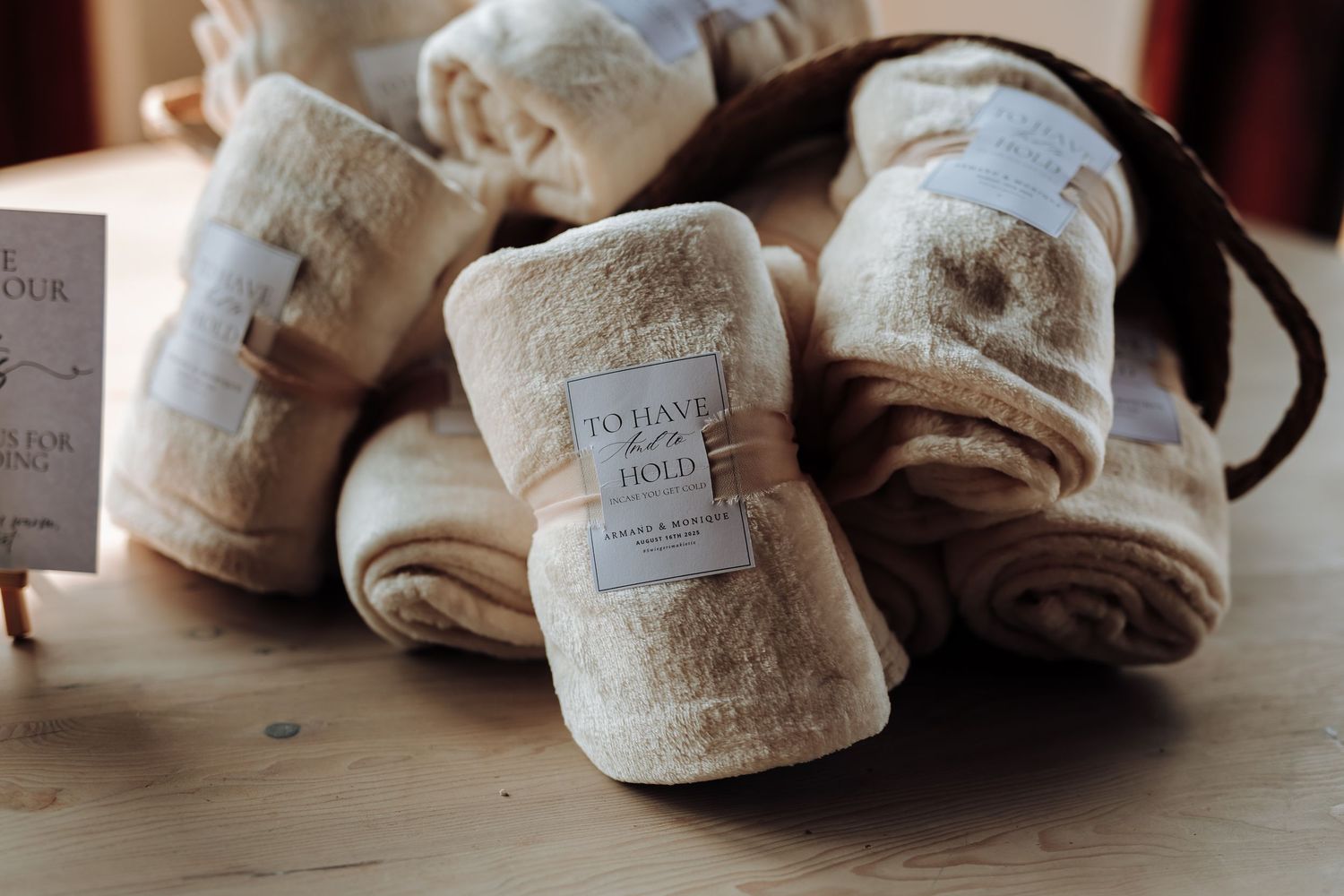 Multiple soft beige throw blankets with tags wrapped in bundles on wooden surface in warm lighting.