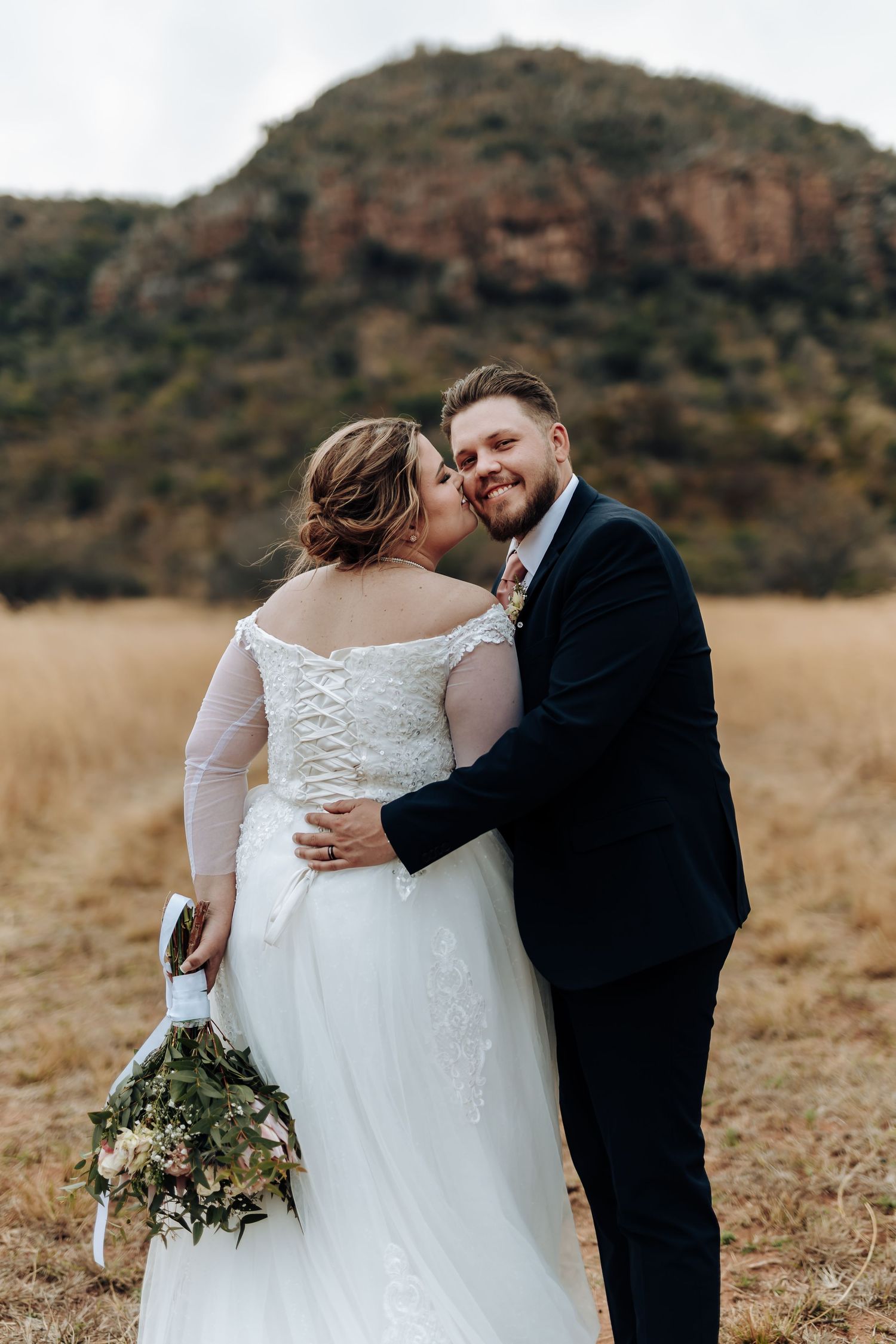 A tender wedding moment captured outdoors with a beautiful mountain backdrop and golden field.