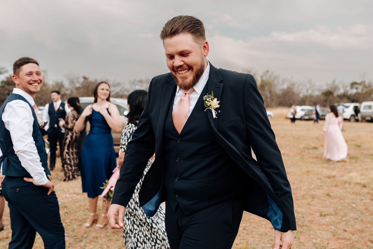 Wedding guests laugh and celebrate at an outdoor celebration in a rustic field setting.