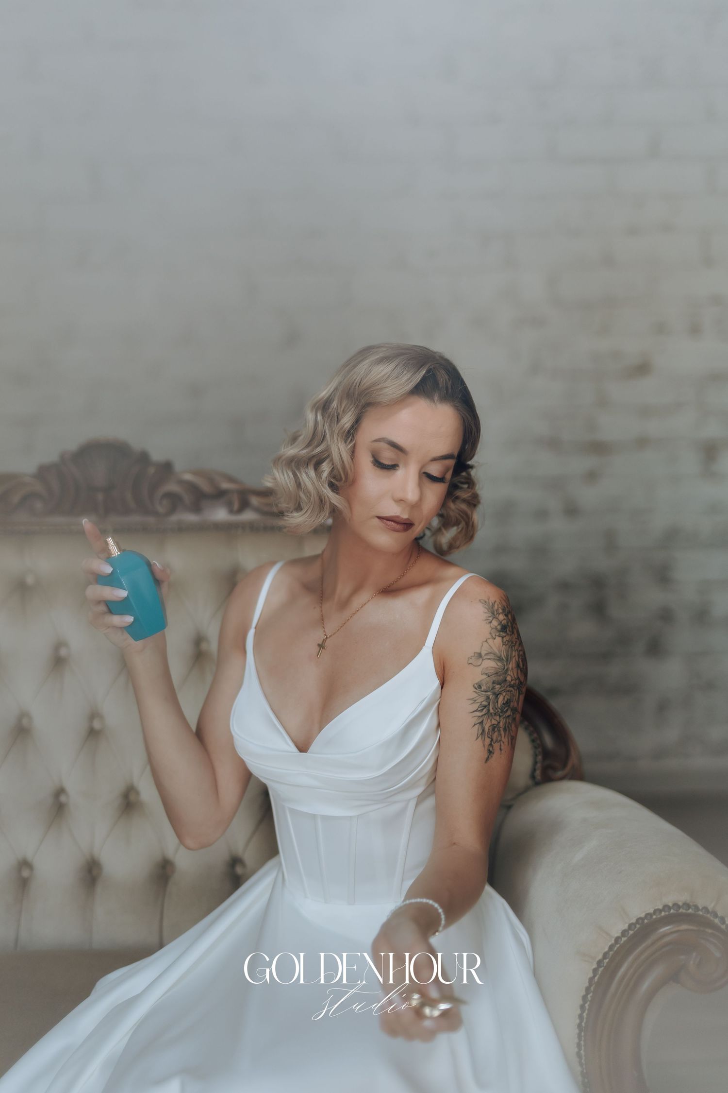 Elegant bridal portrait featuring a white dress and vintage tufted chair in a moody indoor setting.