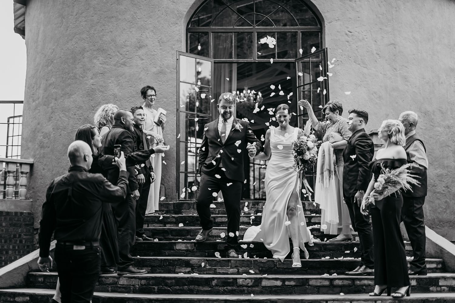 A black and white vintage wedding photograph shows guests throwing confetti as newlyweds descend church steps.