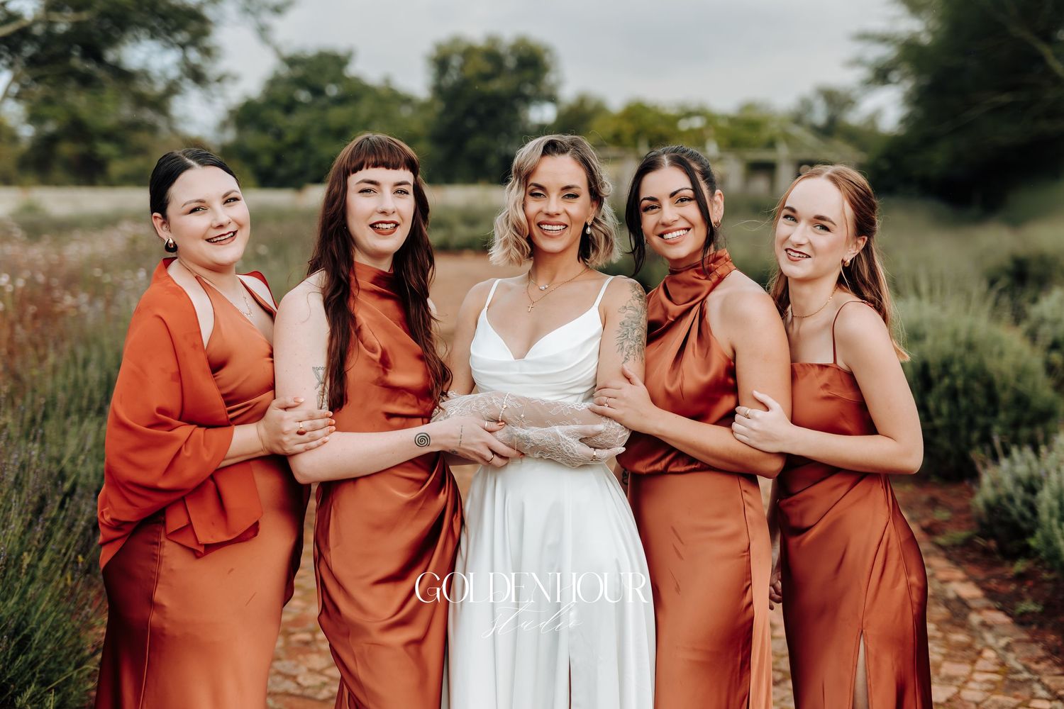 Bridal party in rust-colored dresses posing together outdoors.