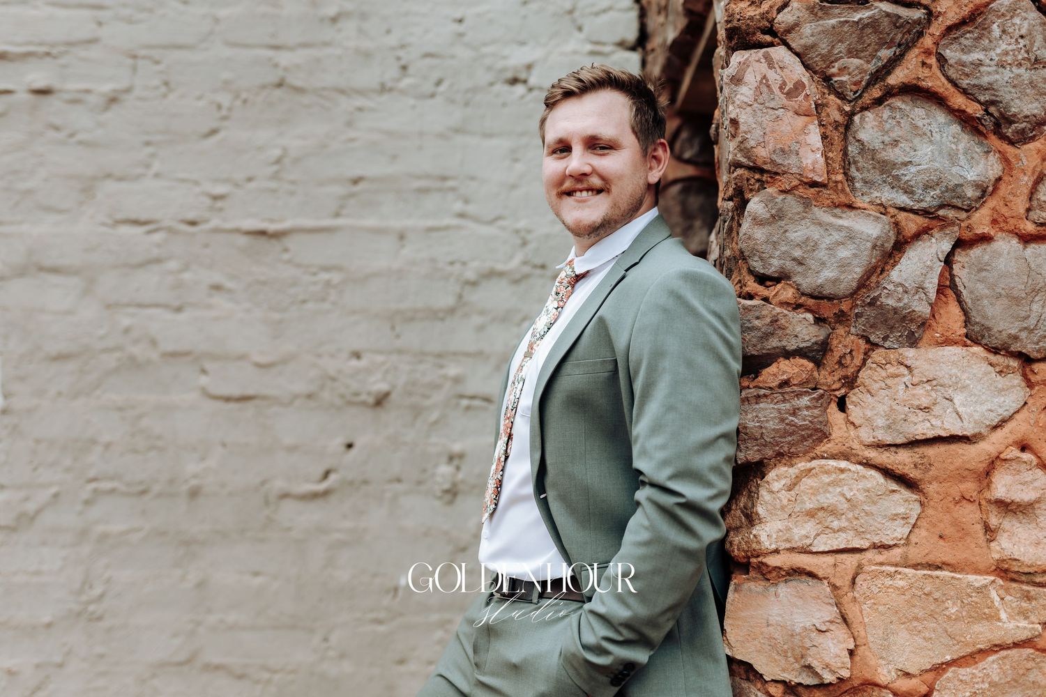 Wedding party poses against a rustic stone wall wearing sage green and white attire.