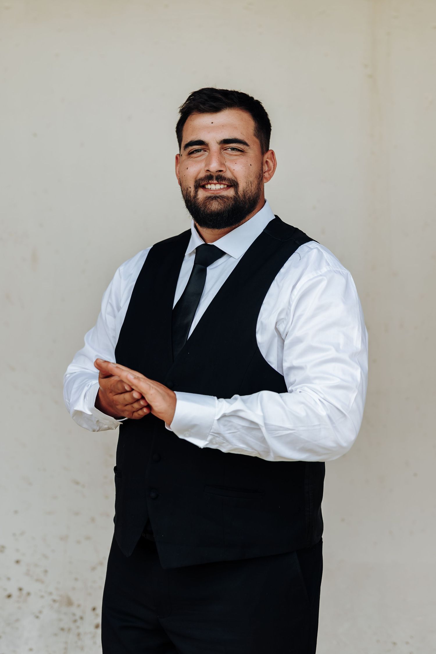 A man in formal attire with black vest and white shirt poses in a sequence of four expressive portraits.