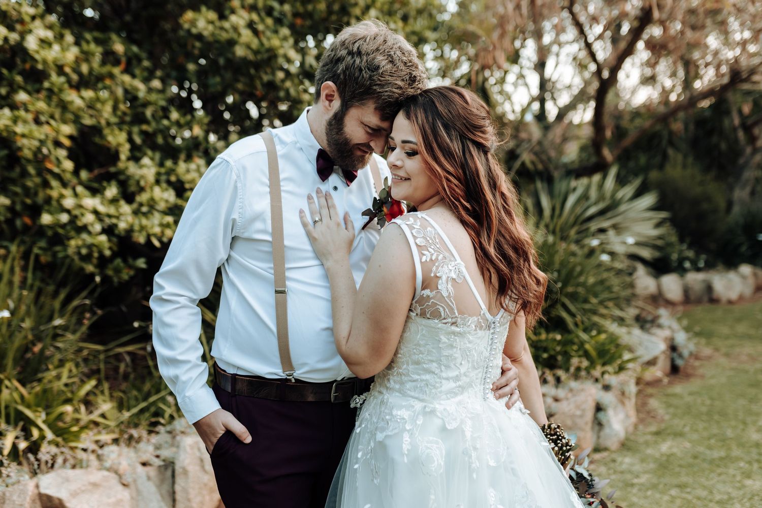 Intimate garden wedding photo with couple in classic white and dark attire.