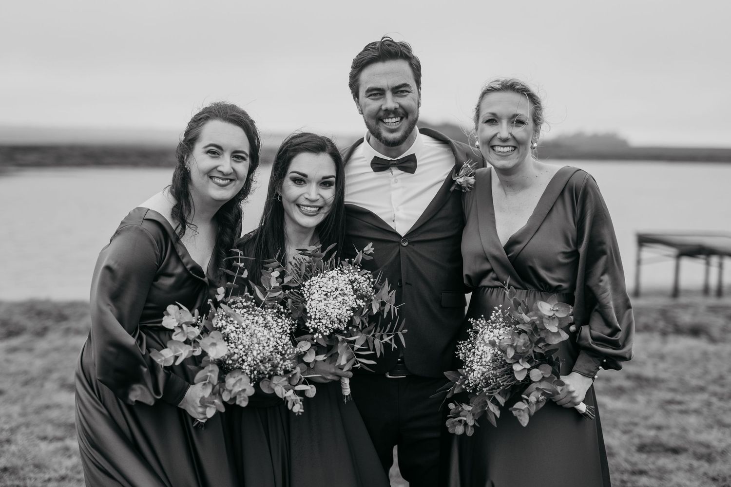 Black and white photo of wedding party posing together by waterfront.