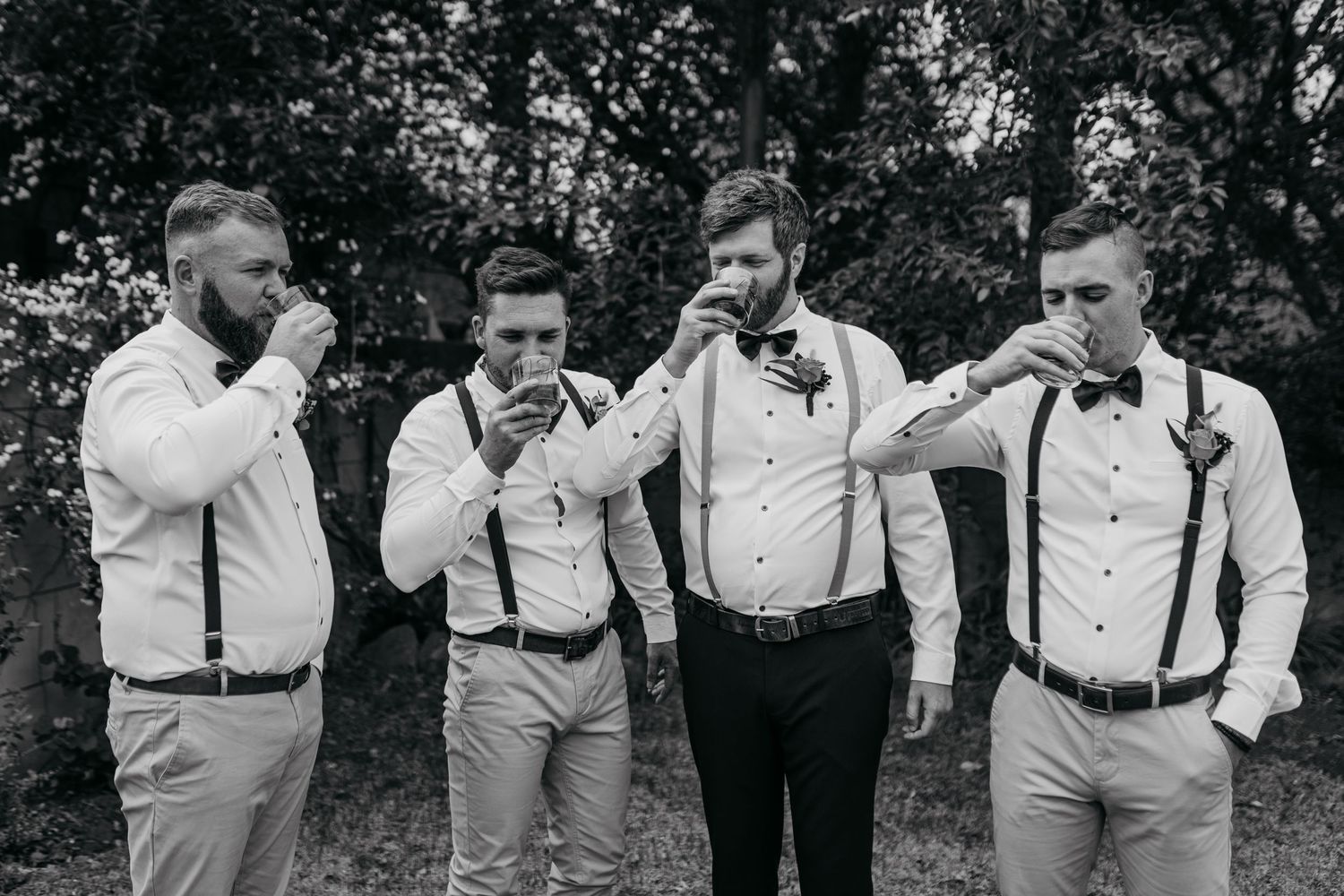 Black and white photo of groomsmen taking shots together in formal attire.
